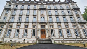 Ein großes, historisches Gebäude mit mehreren Balkonen, einem zentralen Eingang mit Stufen und einer symmetrischen Fassade.
