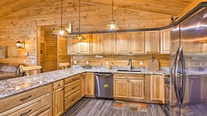 Eine Küche mit Holzschränken, Granit Arbeitsplatten und Edelstahlgeräten, beleuchtet durch Pendelleuchten.