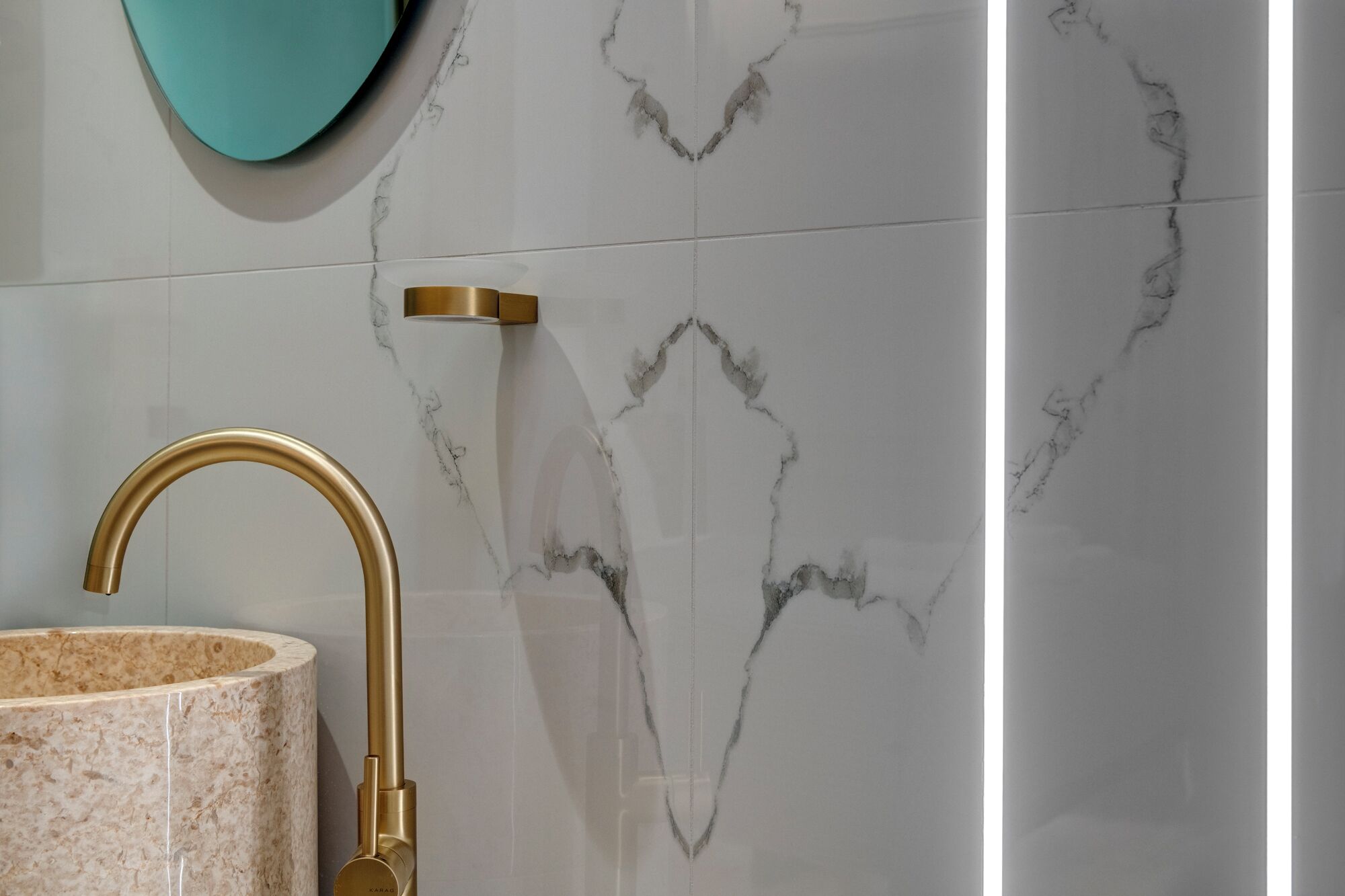 Ein Badezimmer mit goldfarbenem Wasserhahn, einem beige-farbenen Waschbecken und weißen Marmorfliesen mit grauen Adern.