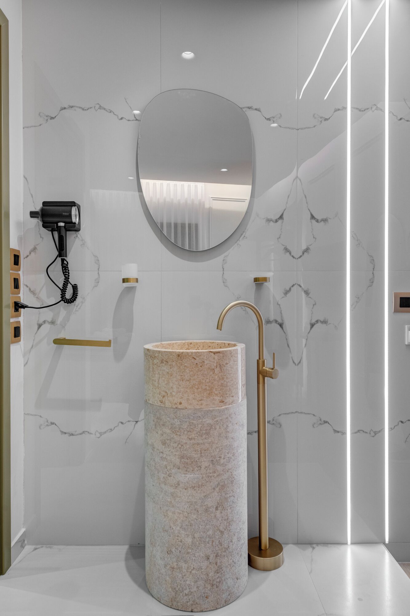 A bathroom with a marble sink, a gold faucet, and a round mirror.