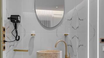 A bathroom with a marble sink, a gold faucet, and a round mirror.
