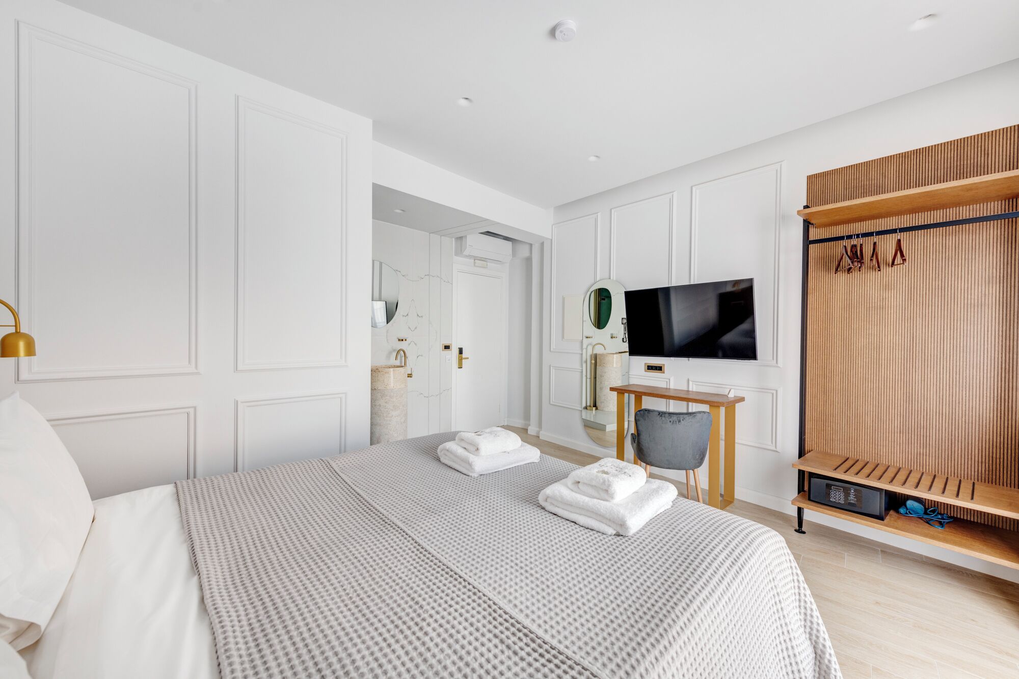 A modern hotel room with a large bed, a TV, a desk, and a wardrobe.