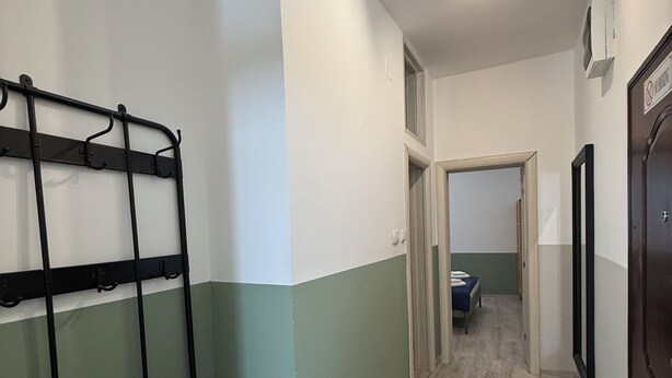 A hallway with a metal bench, a door with a sign, and a bed in the adjacent room. - Nest Ozana (Kotor)