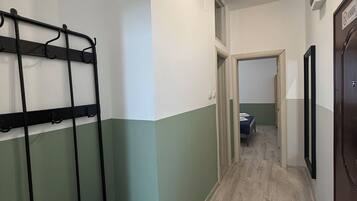 A hallway with a metal bench, a door with a sign, and a bed in the adjacent room.