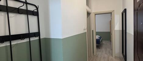 A hallway with a metal bench, a door with a sign, and a bed in the adjacent room.
