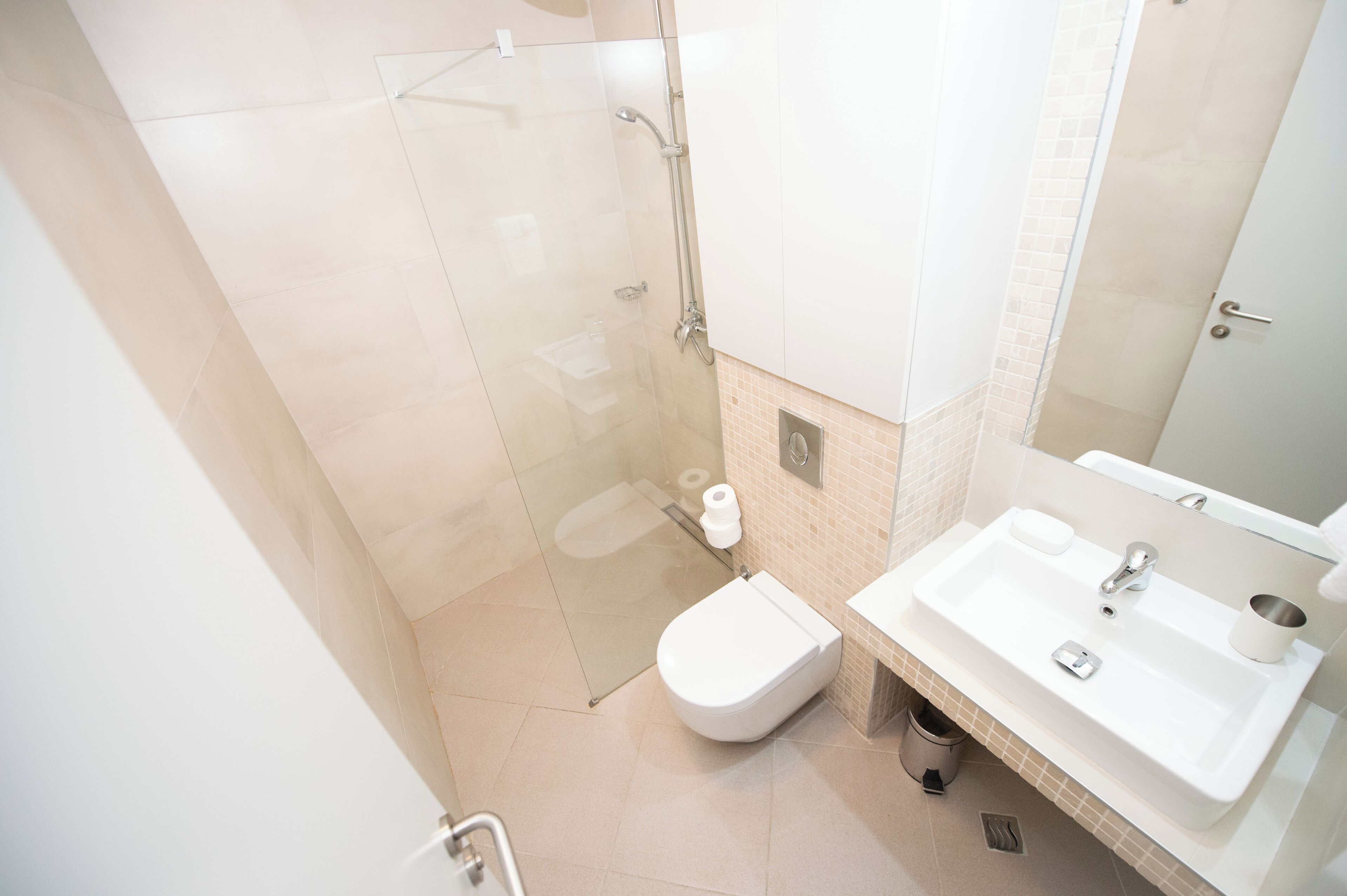 Un baño moderno con ducha de vidrio, inodoro blanco y lavamanos con espejo.