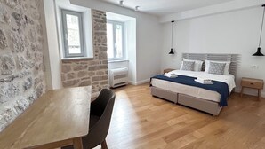A bedroom with a stone wall, a bed with a blue blanket, a wooden desk, and a chair. - Nest Ozana (Kotor)