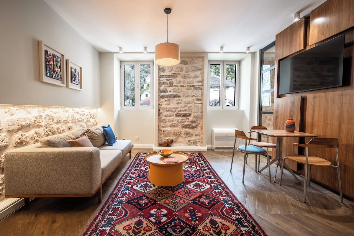 A modern living room with a stone wall, a sofa, a coffee table, and a TV mounted on the wall.
