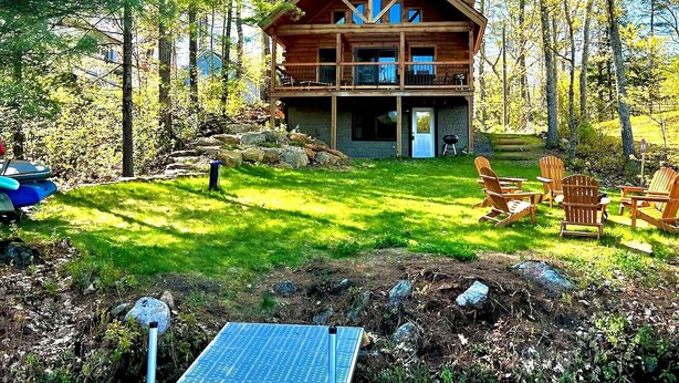 A cabin with a deck, surrounded by trees and a small body of water.
