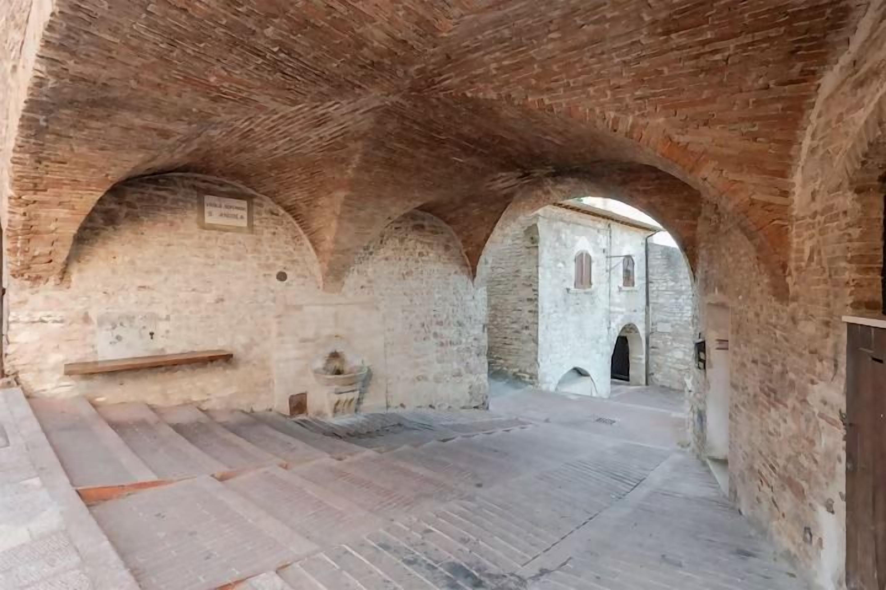An arched corridor with stone walls and a bench.