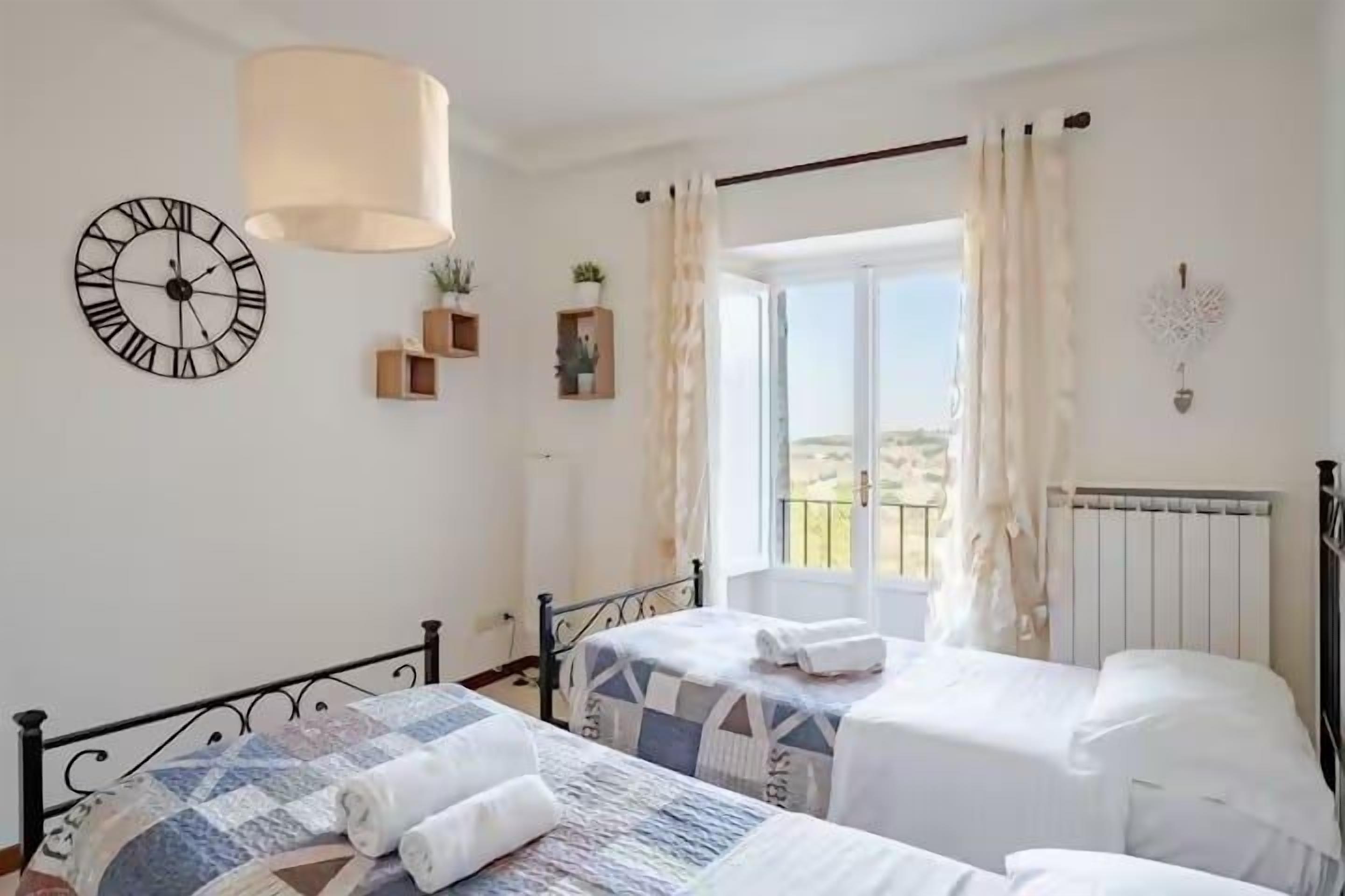 A bedroom with two beds, a clock, a window with curtains, and a radiator.