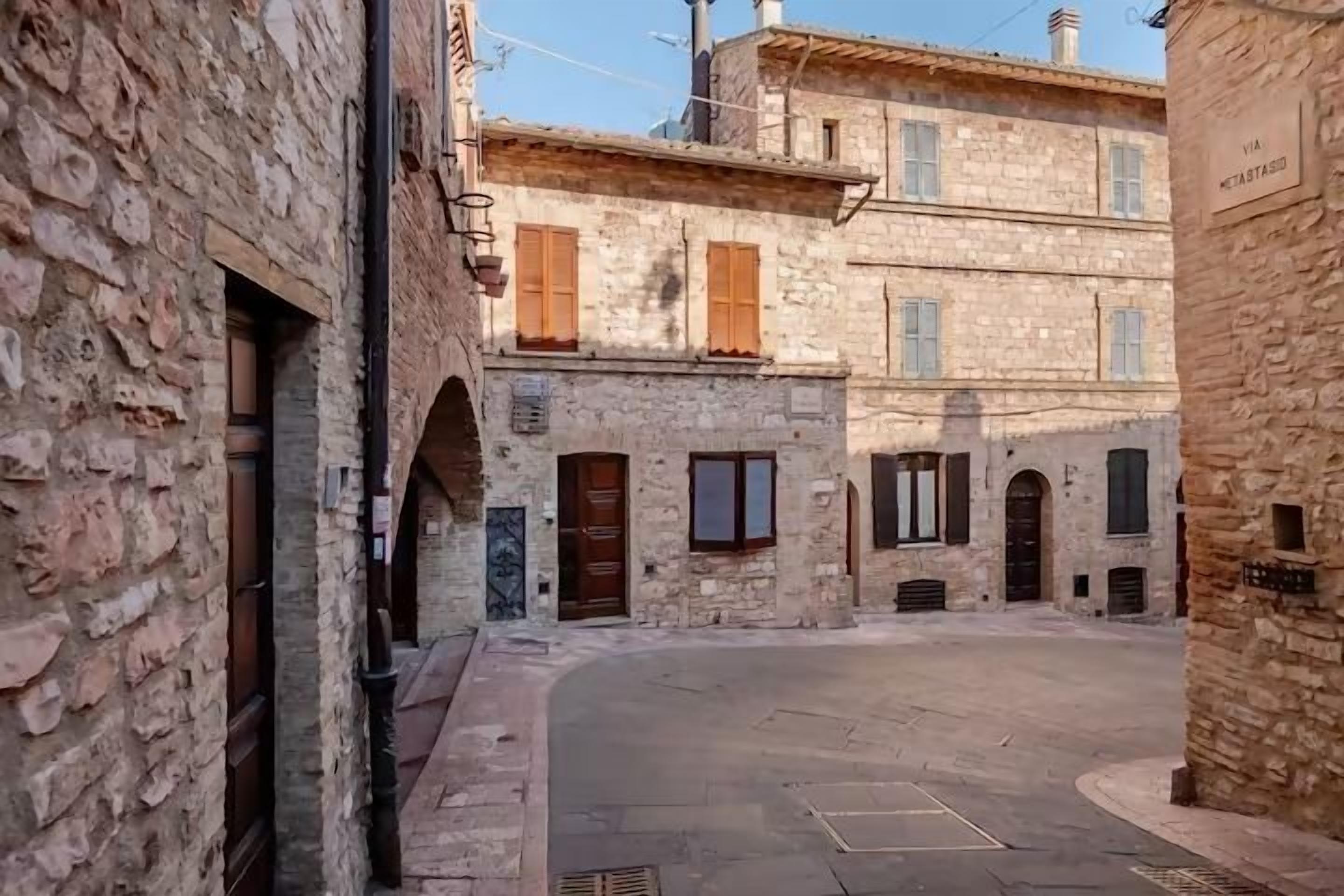 A narrow street with stone buildings, arched doorways, and a clear sky.