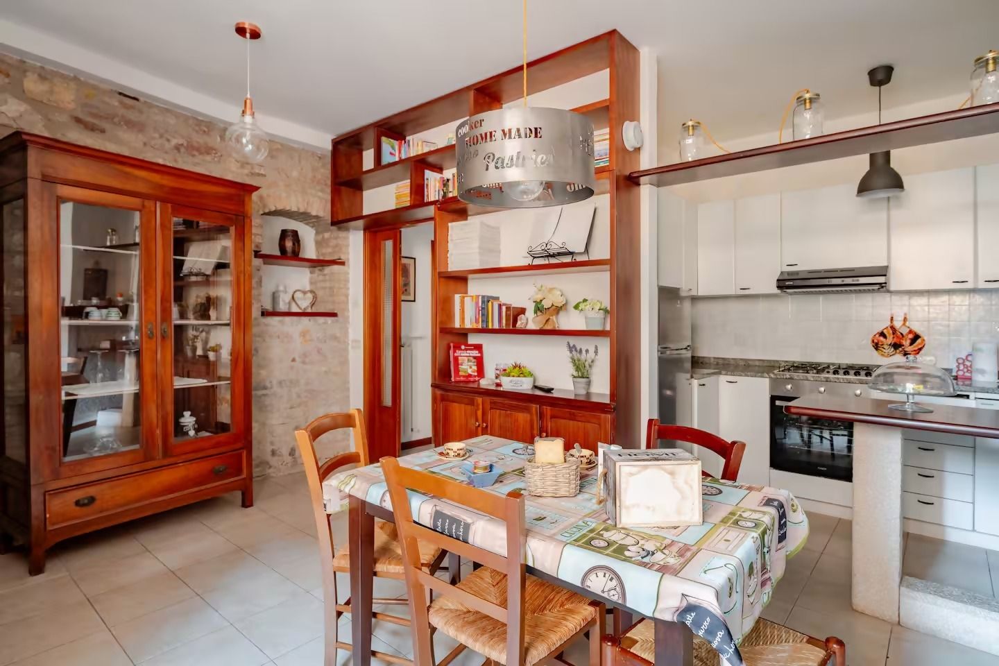 Un comedor con una mesa dispuesta para cuatro personas, rodeada de sillas de madera. Se ve una cocina a la derecha con electrodomésticos modernos.