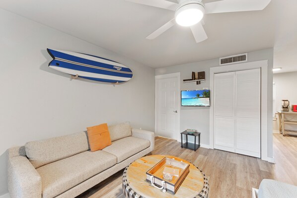 A living room with a sofa, a coffee table, a ceiling fan, a TV, and a closet. - Cozy Studio Large Pool w/ a Private Courtyard and a 5 Min Walk to the Beach (Port Aransas)
