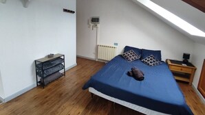 A bedroom with a sloped ceiling, a bed with a blue bedspread, a bedside table with a lamp, and a radiator. - Le Faubourg (Saint-Quentin)