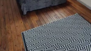 A bedroom with a sloped ceiling, a bed with patterned pillows, a wall-mounted lamp, and a patterned rug. - Le Faubourg (Saint-Quentin)