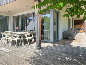 Un espacio exterior moderno para comer con terraza de madera, una mesa con sillas y una silla colgante.