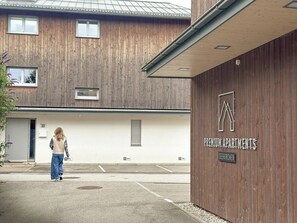 Un edificio con fachada de madera, un cartel que dice "Premium Apartments" y un área de estacionamiento con espacios delimitados.