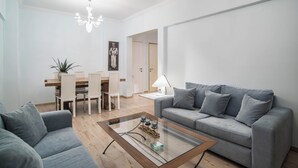 A modern living room with a grey sofa, a glass coffee table, and a dining area with a wooden table and chairs.