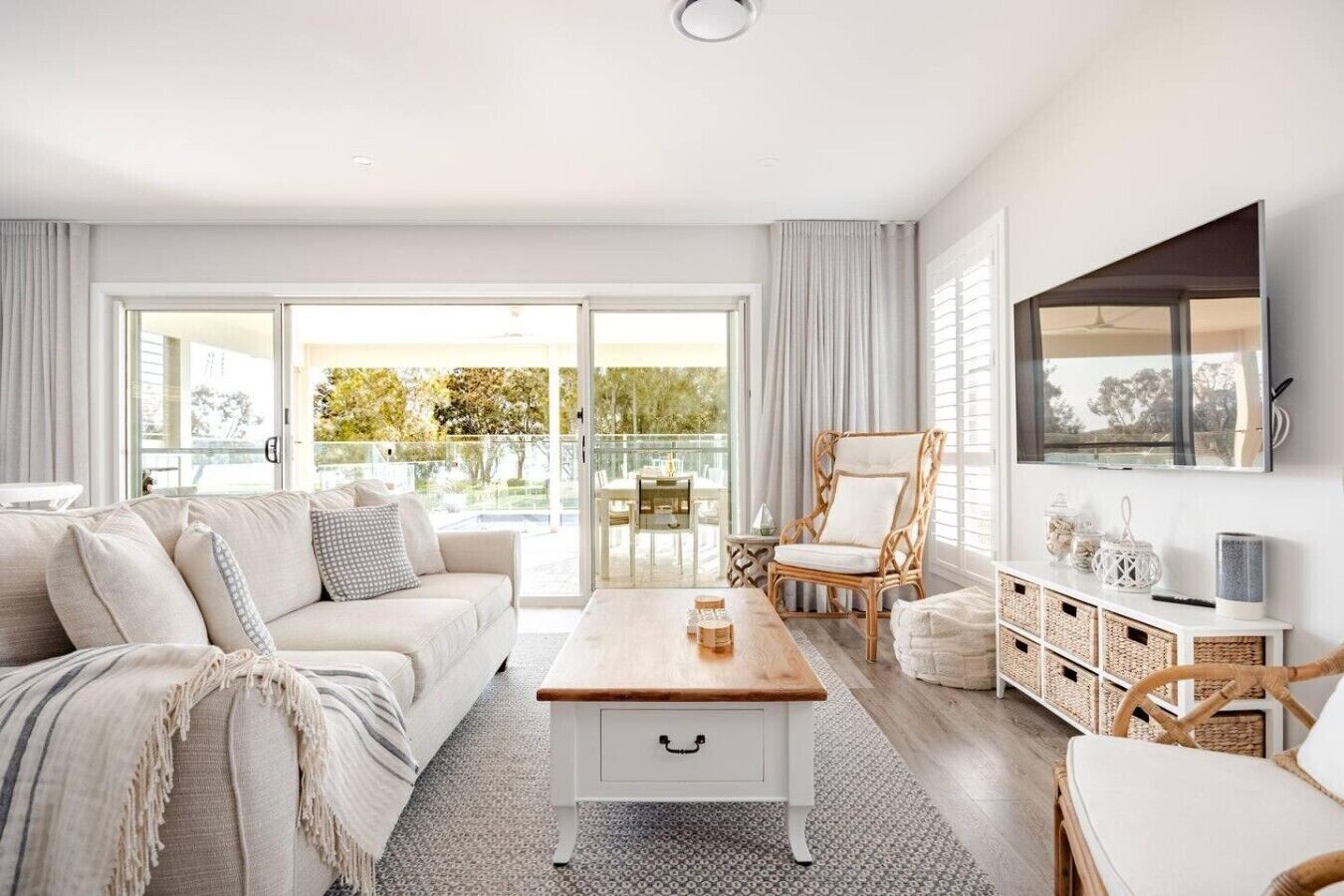 A modern living room with a sofa, coffee table, wicker chairs, and a TV mounted on the wall.