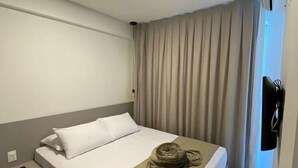 Habitación de hotel con cama, mesita de noche, aire acondicionado montado en la pared y ventana con cortinas.