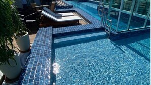 Una piscina infinita en la azotea con sillones de descanso y una planta en maceta.