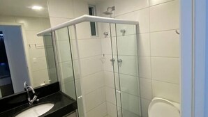 Un baño moderno con cabina de ducha de vidrio, un lavamanos con encimera negra y un inodoro blanco.