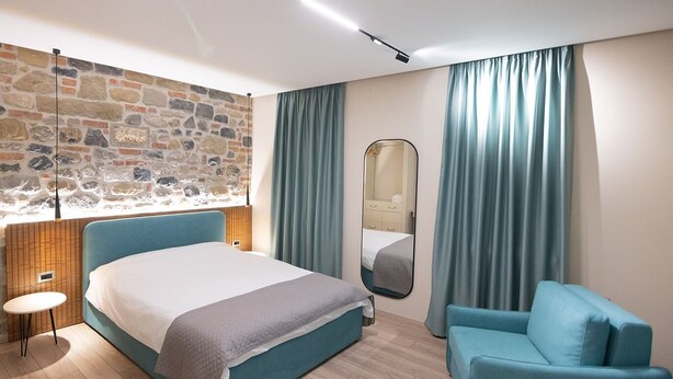 Un dormitorio moderno con pared de piedra, una cama, una silla y un espejo.