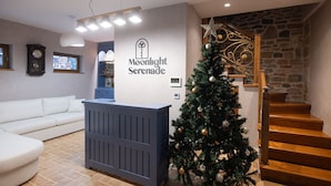 Un área de recepción con un árbol de Navidad, un mostrador de recepción azul, una escalera y una pared de piedra.
