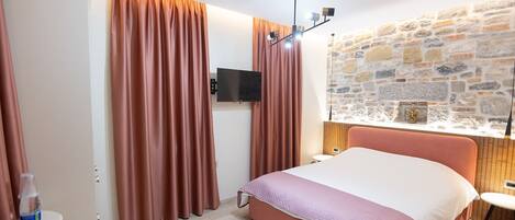 A bedroom with a bed, curtains, a television, a stone wall, and a small table.