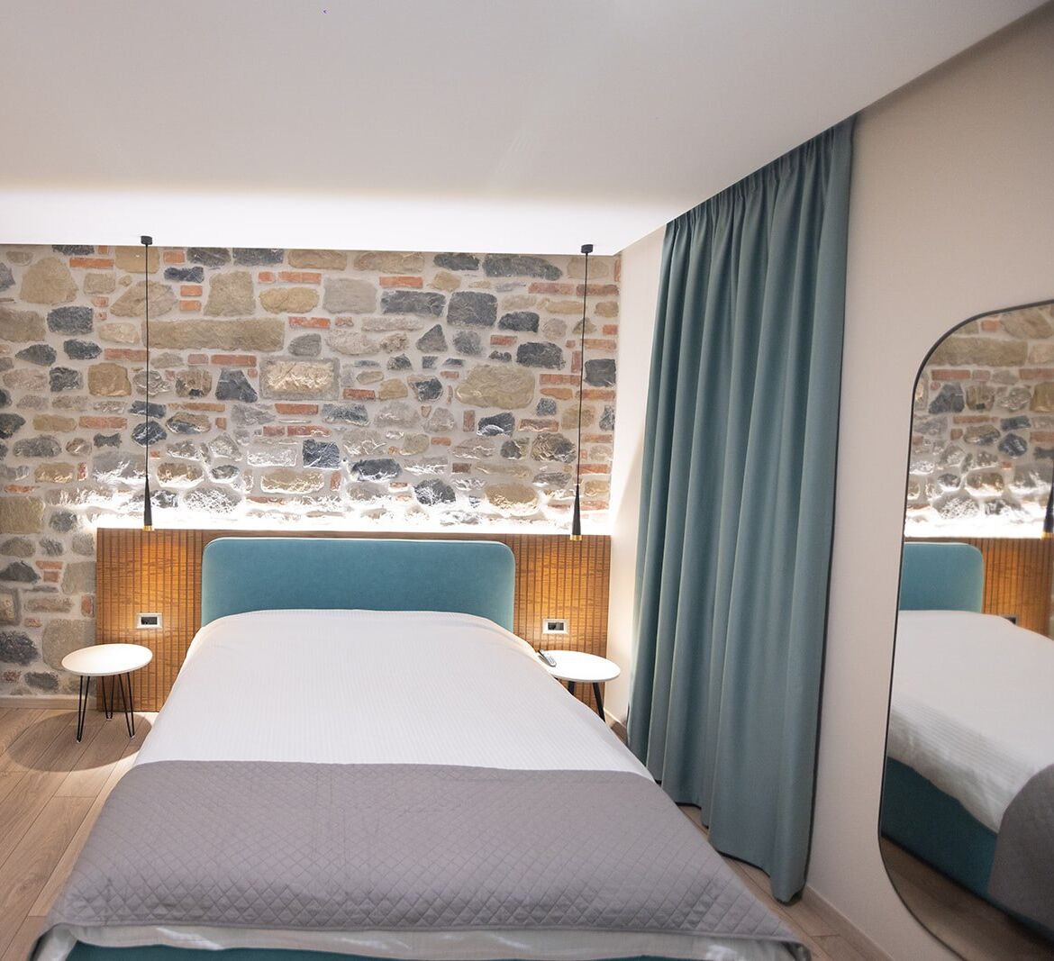 A modern bedroom with a stone wall, a large bed, two bedside tables, and a mirror.