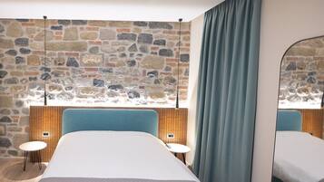 A modern bedroom with a stone wall, a large bed, two bedside tables, and a mirror.