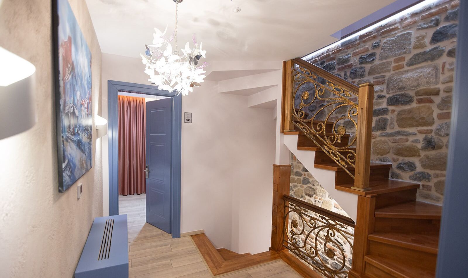 A staircase with a stone wall and wooden steps, a blue door, and a chandelier.