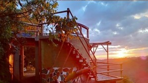 Una estructura de madera rústica con una escalera, rodeada de árboles y una vista al atardecer.