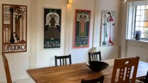 Un coin repas avec une table et des chaises en bois, un bol posé sur la table et trois affiches accrochées au mur.