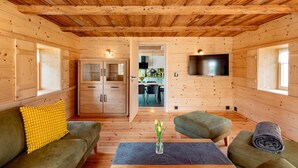 L'intérieur d'un chalet en bois, avec un canapé, un pouf et une table sur laquelle est posé un vase.