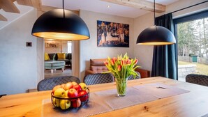 Un coin repas avec une table en bois, un panier de fruits et un vase de tulipes. Deux lampes suspendues noires sont placées au-dessus de la table.