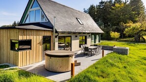 Une maison moderne dotée d’un toit en pente, de grandes fenêtres et d’un patio aménagé avec du mobilier d’extérieur.