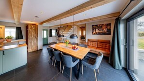 Une cuisine moderne avec un plafond en bois, un coin repas avec une table et des chaises en bois, et une grande fenêtre avec des rideaux.