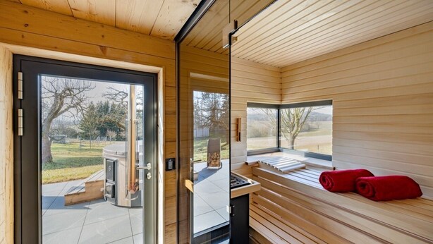 Un intérieur moderne en bois, avec une porte-fenêtre coulissante donnant sur un espace extérieur, un banc avec des serviettes rouges et une vue sur le paysage.