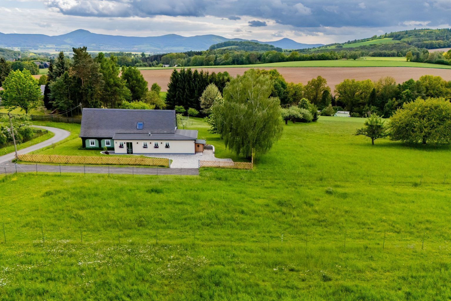 A rural house with a paved driveway and a large lawn.
