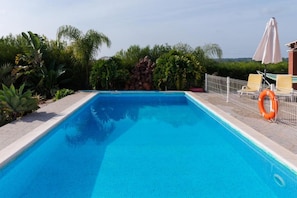 A rectangular swimming pool with clear blue water, surrounded by a white fence, and featuring a lifebuoy and a hammock chair.