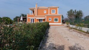 A two-story house with a sandy driveway and a garden.