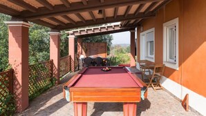 A pool table under a wooden pergola with a brick wall and outdoor seating area.