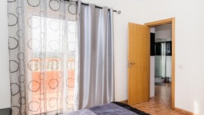 A bedroom with a bed, a wooden door, and a view of a hallway.