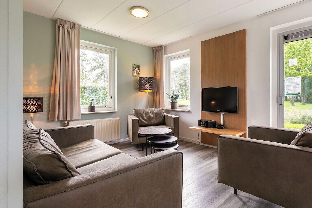 Een moderne woonkamer met een bank, fauteuils, een salontafel, een televisie en uitzicht op de omgeving.