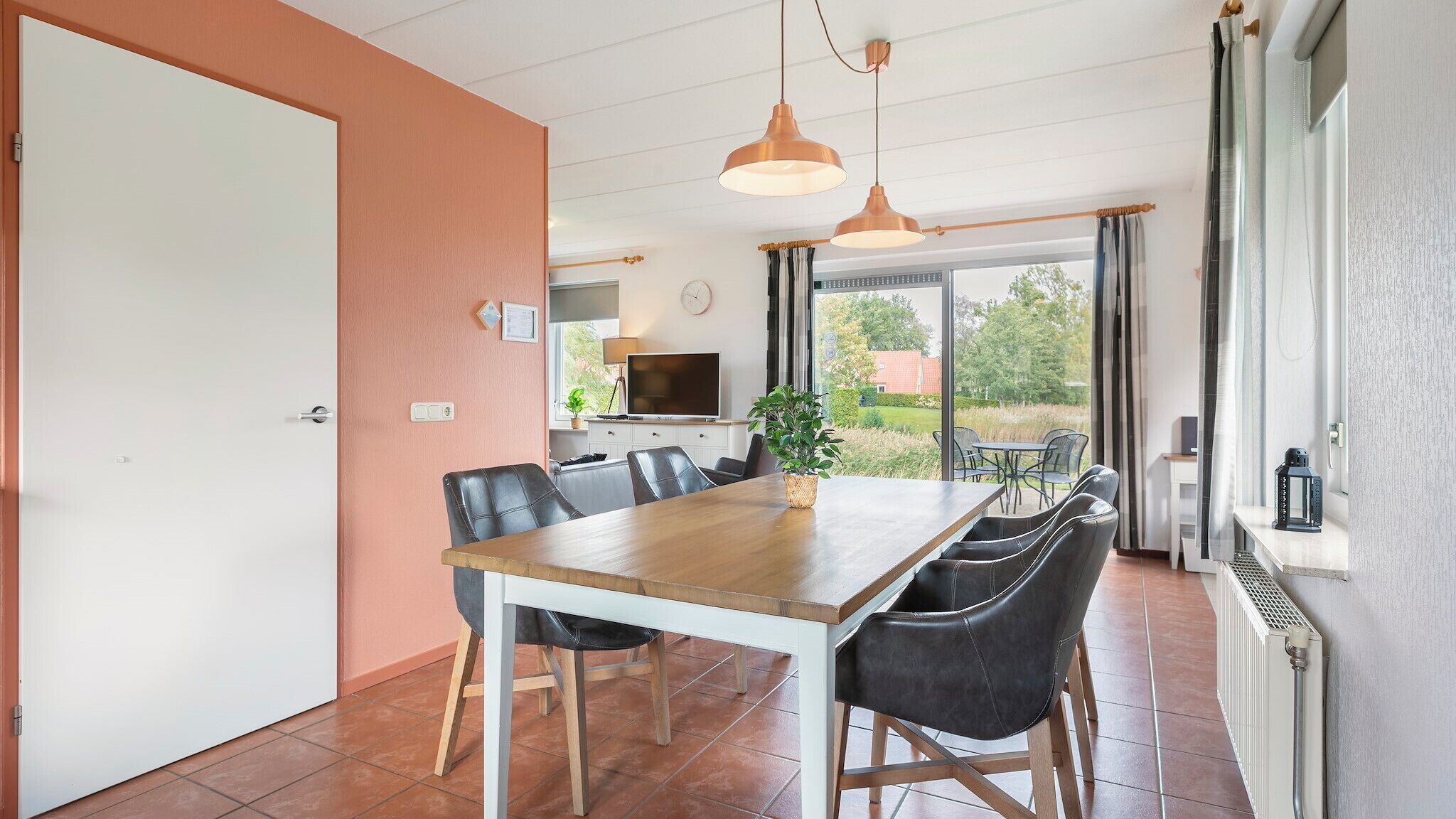A dining area with a wooden table and black chairs, a TV, and a view of the outdoors.