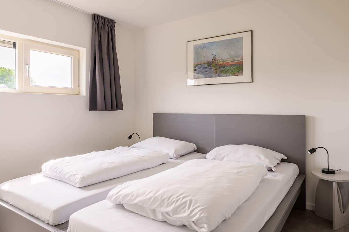 Een tweepersoonsbed met witte lakens en een grijs hoofdeinde in een hotelkamer.