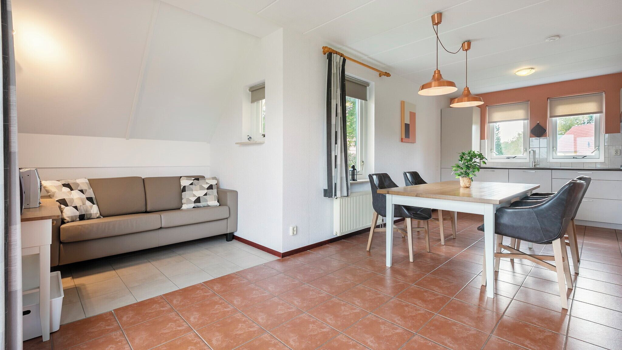 A modern kitchen with a dining area, featuring a sofa, a table with chairs, and pendant lighting.