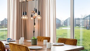 Un comedor con una mesa de madera preparada para dos personas, una planta en maceta y una lámpara colgante moderna.